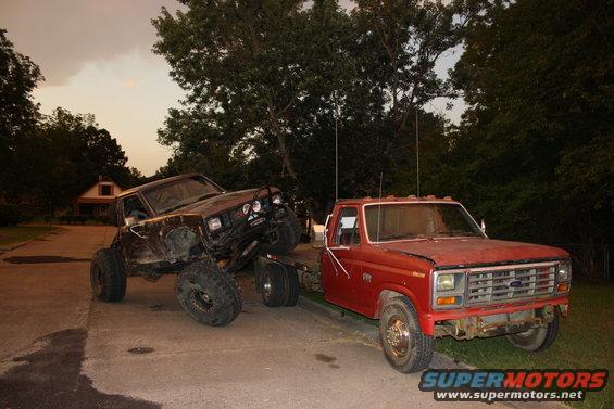 Red Ford F-Series pickup truck towing a heavily modified dark SUV with large tires