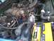 1995 Ford Bronco - Close-up view of an engine bay, a yellow battery and intricate network of hoses and electrical wiring.