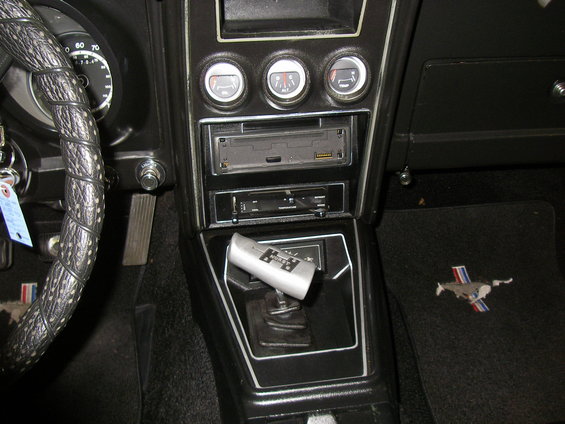 1971 Ford Mustang interior with a black dashboard, three gauges, a car stereo, a floor shifter, and a floor mat with a running horse logo