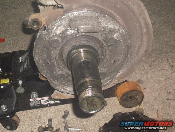 Front wheel hub assembly with bearing race and spindle, resting on a floor jack. Some bolts are scattered nearby