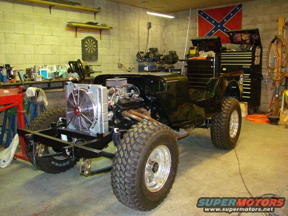 Jeep CJ-5 body with engine and radiator installed, in a garage. Front tires are large off-road type