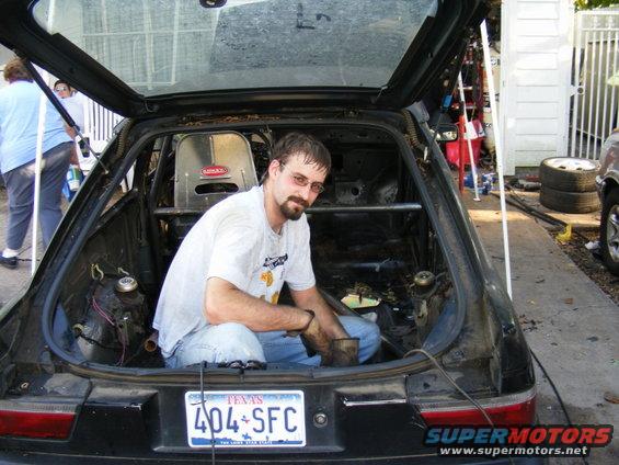 Man sitting in the back of a stripped-out car with a roll cage and racing seat. Texas license plate visible