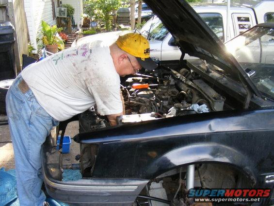 Black 1989 Ford Escort with hood open, man working on engine. Front view