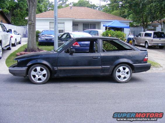 Black hatchback car parked on street, house and other cars in background