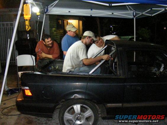 Four guys working on the interior of a black car with a roll cage installed