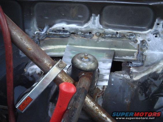 Close-up of rusty metal frame with fresh welds and a red-handled tool