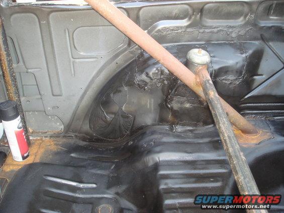 Interior of a car trunk with black undercoating and a roll bar. A can of spray paint is on the left
