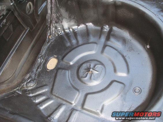 Spare tire well with black undercoating and some rust