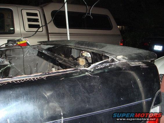 car trunk area with exposed metal and a spoiler, truck in background
