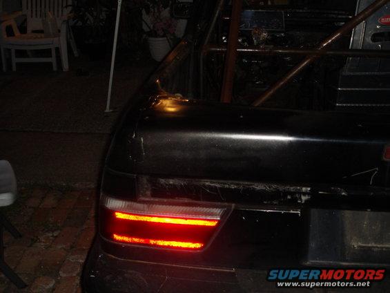 Black car trunk with a red taillight illuminated, roll cage visible inside
