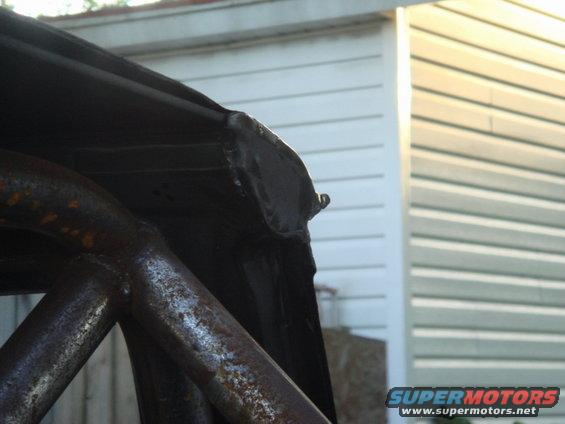Close-up of a rusty roll cage tube and the edge of a black car roof