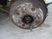 1989 Ford Escort - Close-up of a rusty wheel hub and brake drum assembly, showing lug studs and a central nut.