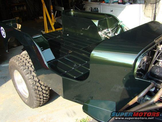 Dark green Jeep CJ-3A body, showing the flatbed and front fender with a star emblem. Engine and exhaust visible