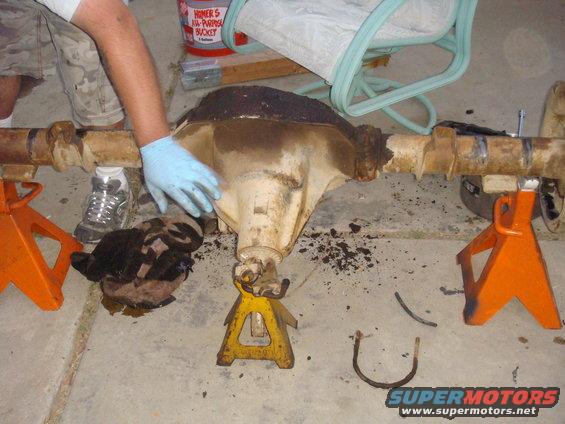 Differential axle assembly on orange and yellow jack stands, with a gloved hand touching it