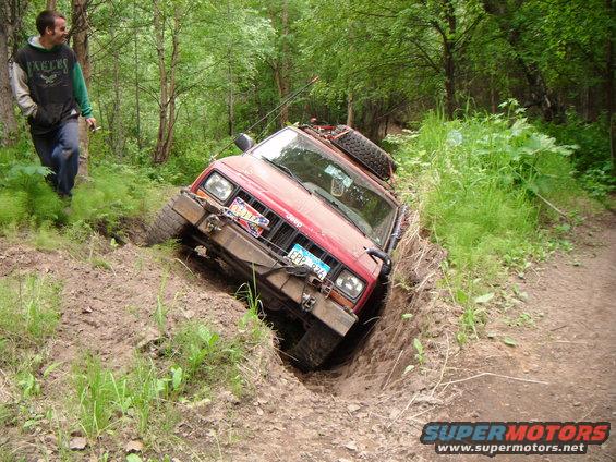 Red 1998 Jeep Cherokee tilted in a ditch with a man watching