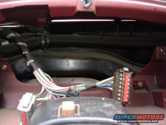 Close-up of a red dashboard interior showing a complex wiring harness with multiple connectors and black corrugated tubing