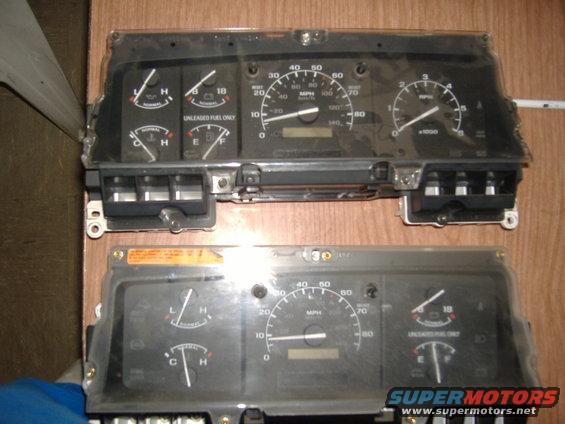 Two automotive instrument clusters, one above the other, on a wooden surface