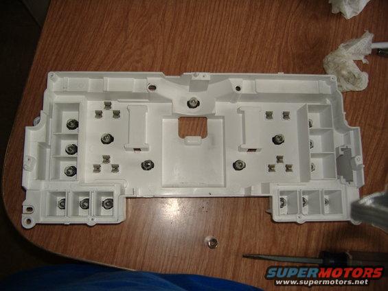 White plastic housing for a vehicle's instrument cluster, showing mounting points and electrical connectors