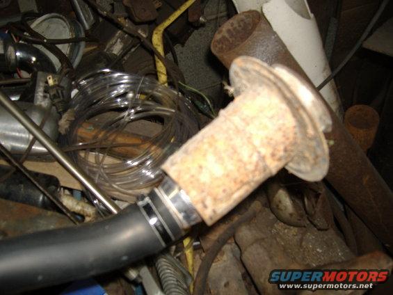 Close-up of a rusty exhaust pipe fitting connected to a black hose, surrounded by various wires and metal parts