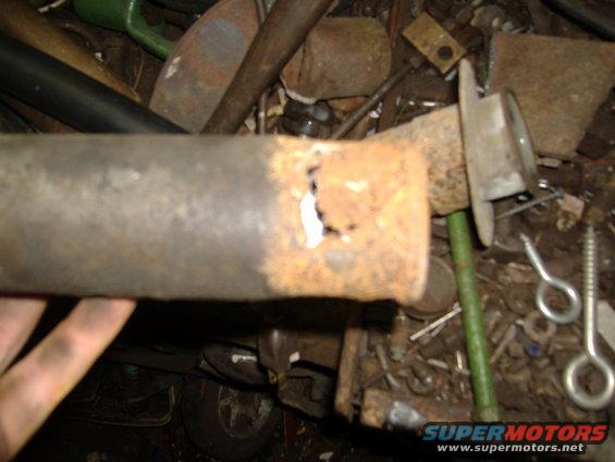 Rusted exhaust pipe with a hole, held by a hand, with a vehicle wheel visible in the background