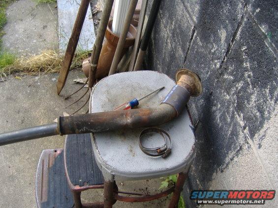 Exhaust pipe with a screwdriver and hose clamp on a stool, leaning against a cinder block wall