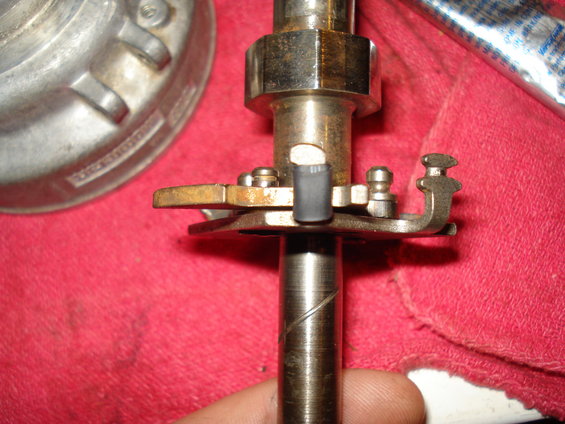 Close-up of a distributor shaft with points and a small gray condenser. A metal housing is to the left