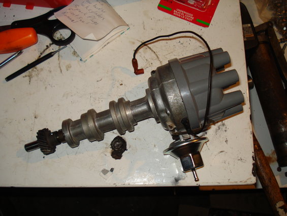 Distributor assembly with wires and vacuum advance, on a workbench with tools and a note