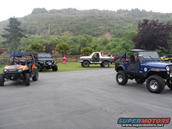 Several off-road vehicles parked in a lot, including a blue Jeep, a white Ford truck, and an orange ATV