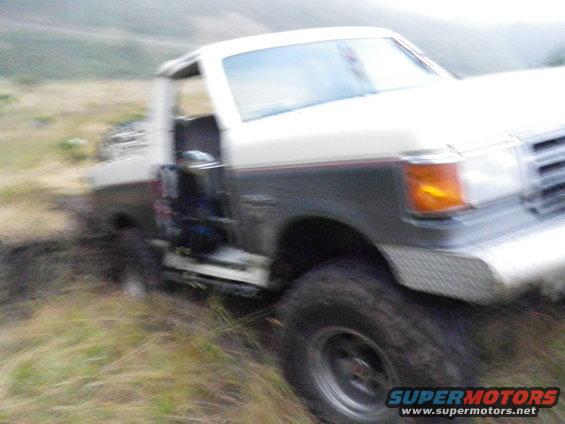 Pickup truck with open door stuck in mud on a grassy hill