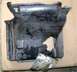 1972 Ford Ranchero - This is a damaged plastic part, possibly from a vehicle's undercarriage, with a large hole and detached foil.