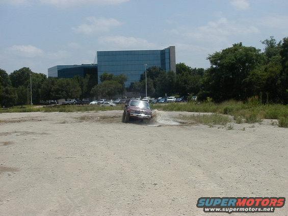 Red SUV driving through a muddy puddle, front view. The vehicle appears to be from the mid-1990s