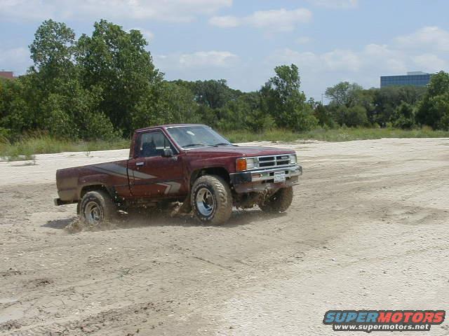 Maroon pickup truck with side graphics driving in dirt