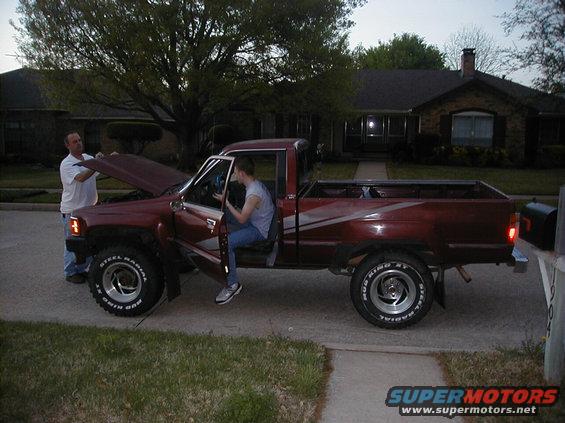 Red pickup truck with two people, hood up, driver's door open