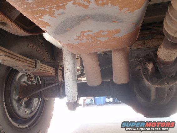 Underside of a vehicle showing dual exhaust pipes, leaf springs, shock absorber, and rear axle