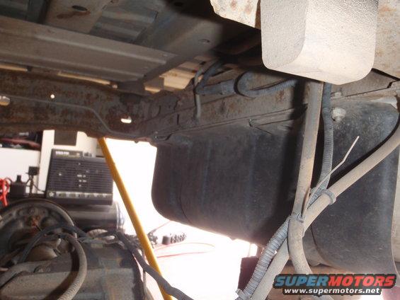 underneath a vehicle showing the fuel tank and frame rails, with some rust visible