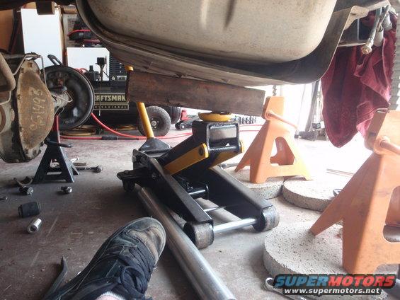 Vehicle being lifted by a jack and supported by jack stands, with a person's foot visible