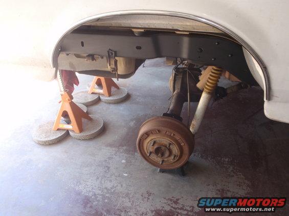 White vehicle's rear axle and suspension on jack stands, showing rusty drum brake