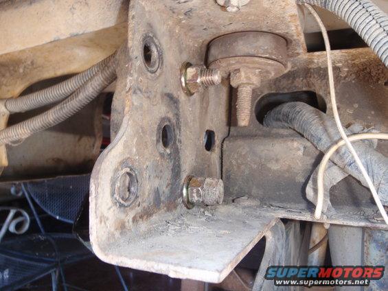 Close-up of a rusty metal bracket with bolts and wiring harnesses attached