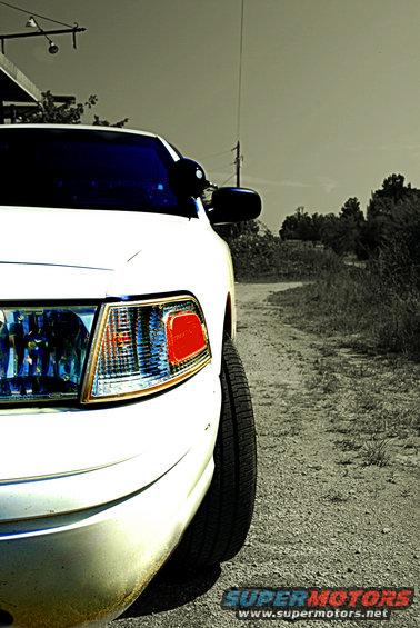 Front corner of a white 2002 Ford Crown Victoria parked on a dirt road