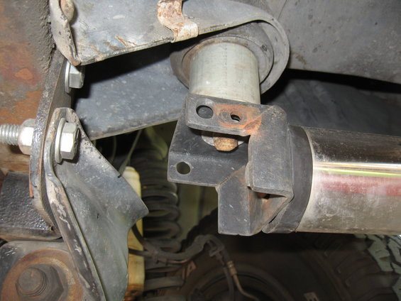 Close-up of a nerf bar mounting bracket attached to rusty vehicle frame, with suspension spring visible
