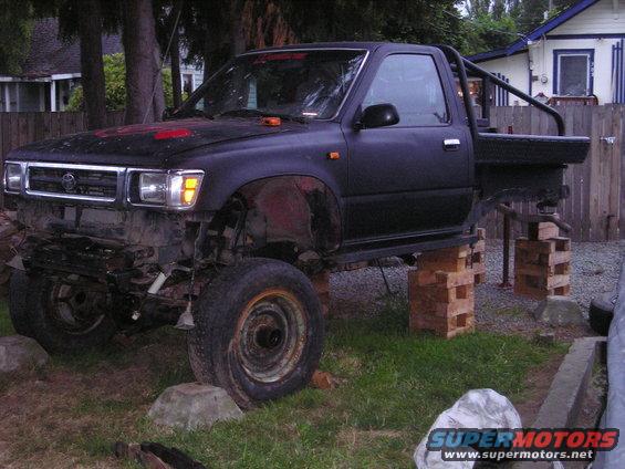Black Toyota pickup truck on blocks, front bumper removed, roll bar in bed