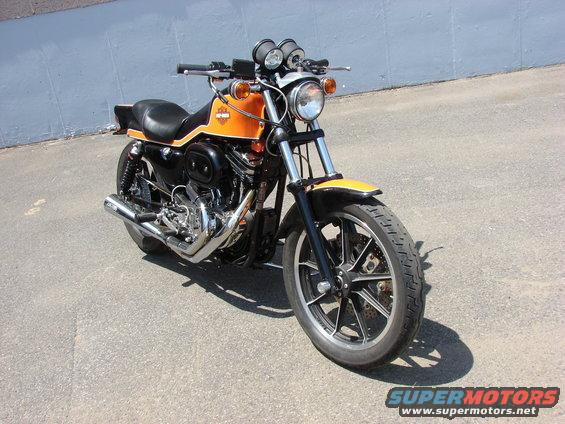 Orange and black motorcycle parked on pavement, front wheel and engine visible