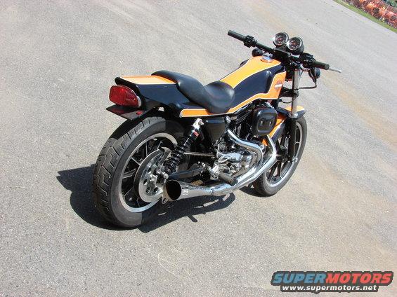 Black and orange motorcycle, rear three-quarter view, parked on asphalt