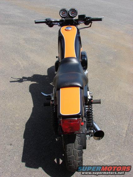 Rear view of a black and orange motorcycle with dual gauges on the handlebars