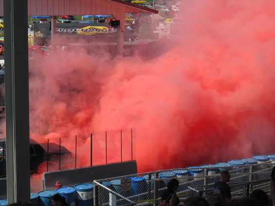 Black car emitting large cloud of red smoke at a track event