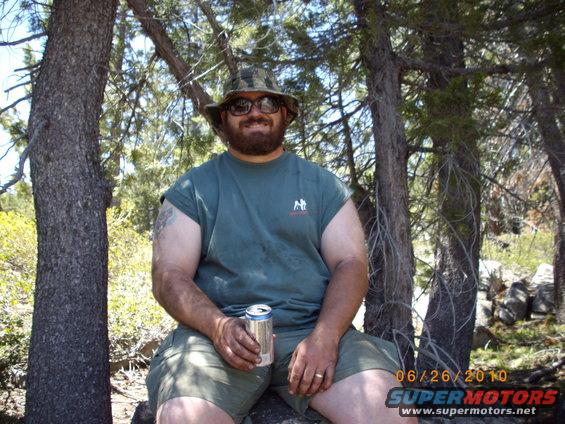 Man with beard and hat holding a can, seated outdoors