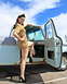 1963 Ford F-100 - A woman in a vintage military-style uniform poses next to a classic light blue pickup truck on a sunny day.