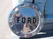 1963 Ford F-100 - A chrome hubcap with the Ford logo is shown against the backdrop of a blue vehicle's fender.