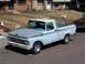 1963 Ford F-100 - This light blue Ford pickup truck features a two-tone paint scheme with a gray hood and a white roof, parked on a street with a house in th…