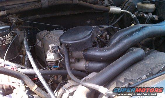 Engine bay with hoses and engine components visible. A "CAUTION" label is partially visible